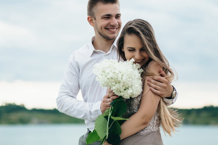 Casal rindo abraçado, com um buquê de hortênsias brancas