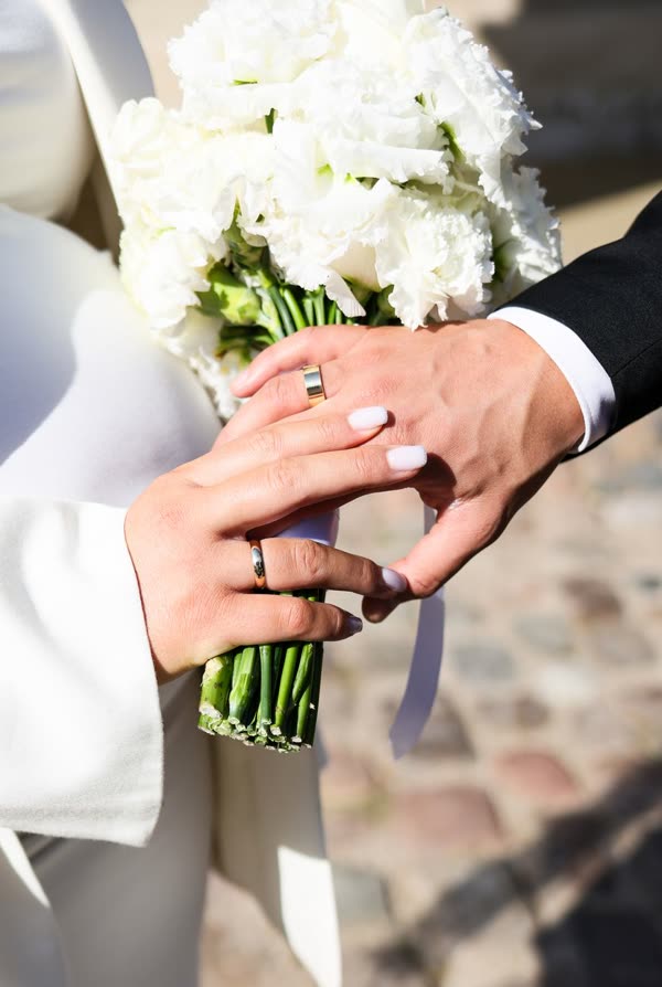 Mãos do casal com alianças e buquê